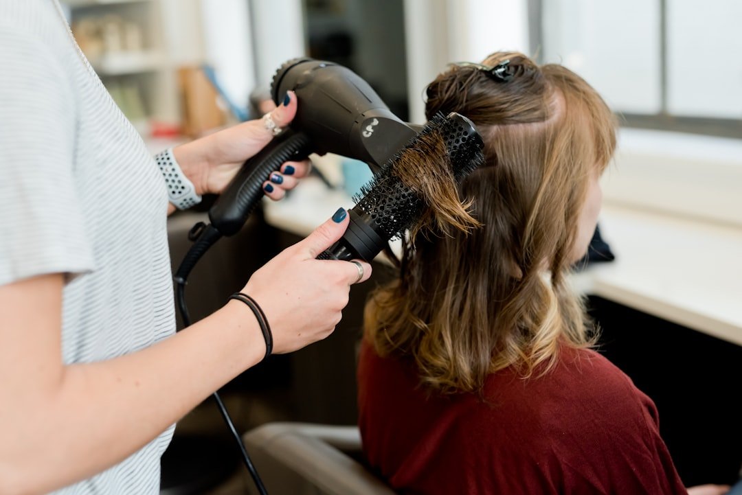 A hairstylist using a blow dryer and round brush on a client's hair