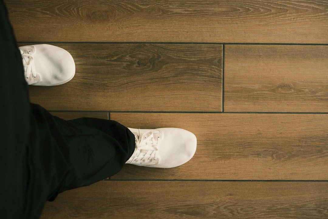 A person wearing white sneakers walks on a wooden floor