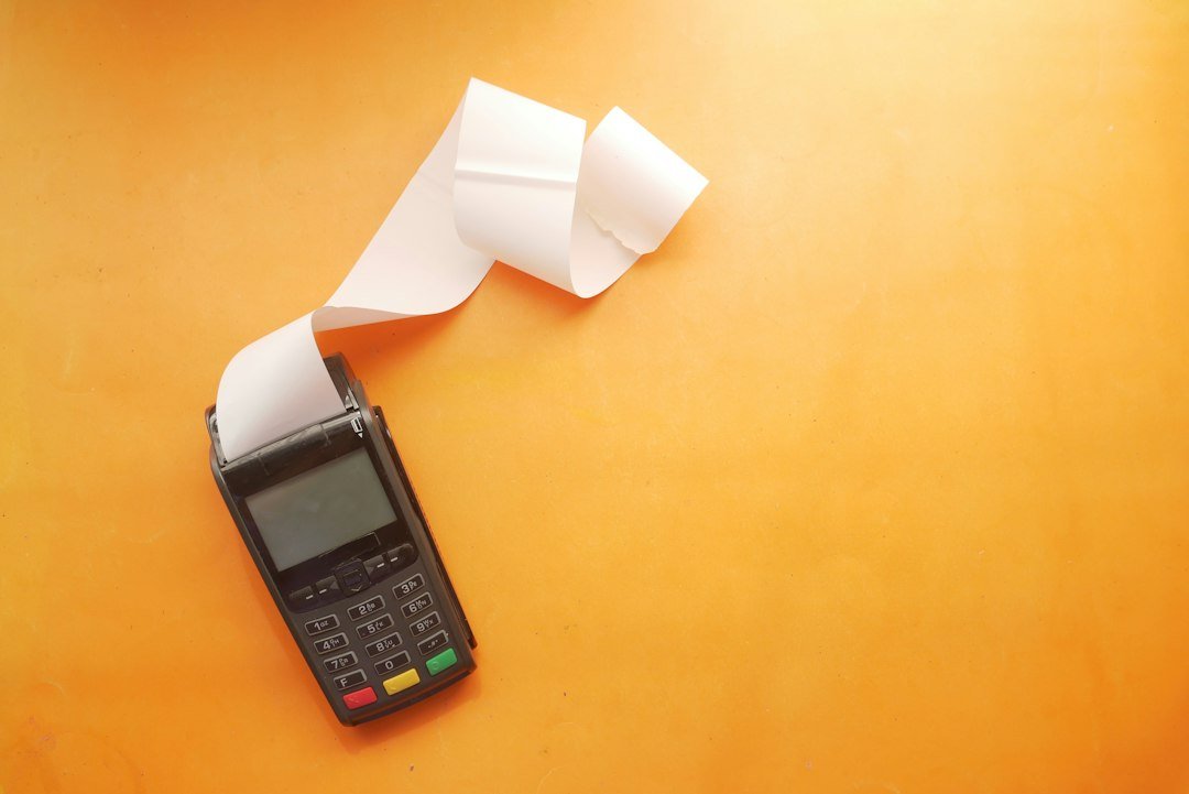 A payment terminal with a paper receipt roll on an orange surface